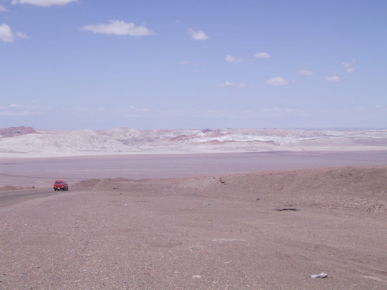 Red truck descending a long hill into a dry valley in the Atacama Desert, low barren mountains in the background